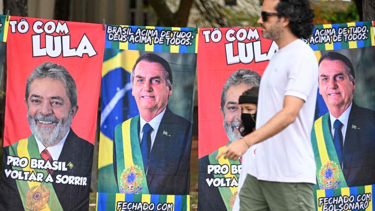 Un hombre camina junto a carteles electorales de Lula y Bolsonaro, en una calle de Brasilia.