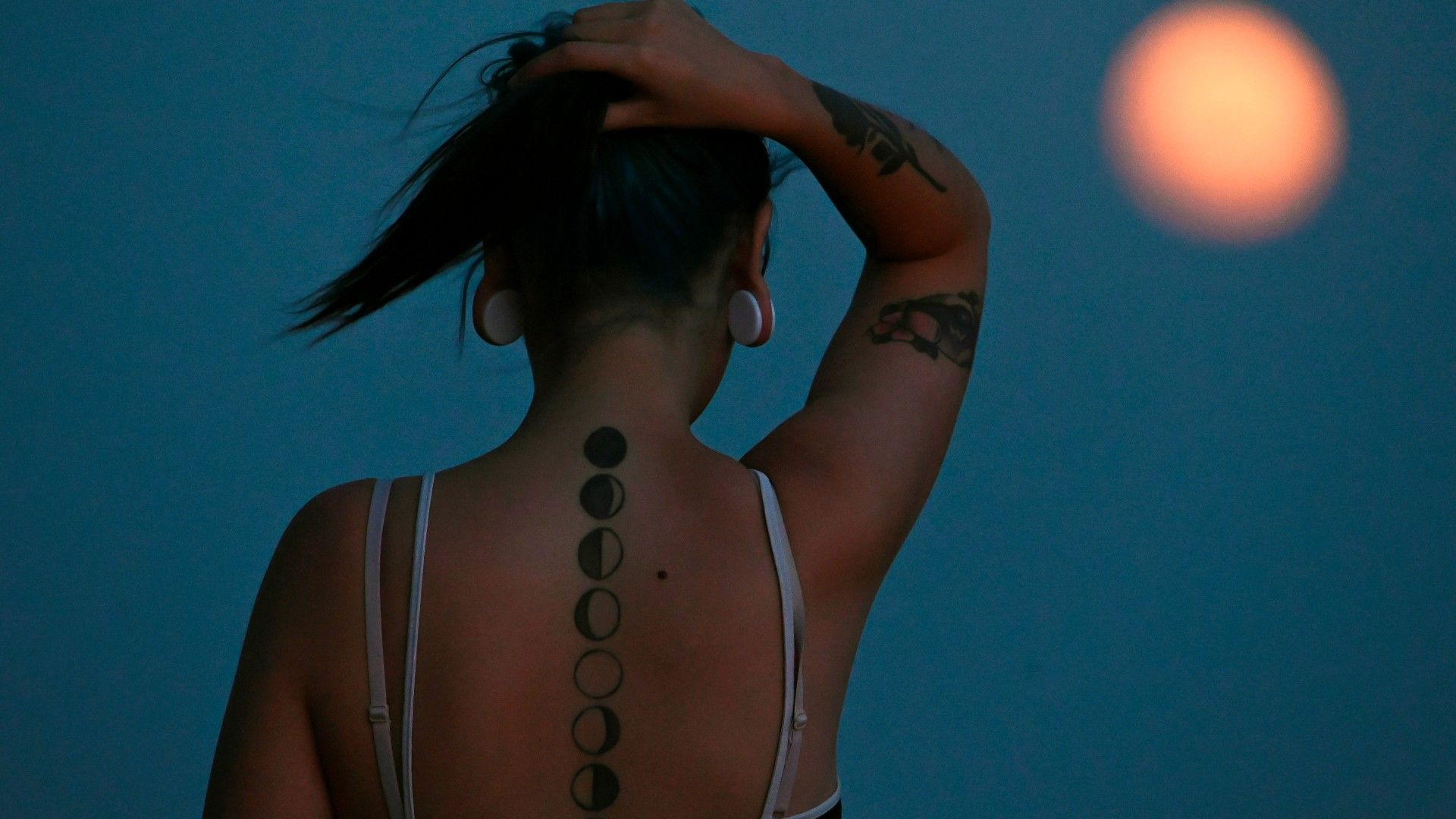 Una joven observa la luna del ciervo de julio del año pasado en Madrid, mostrando un tatuaje con las fases de la luna en su espalda.