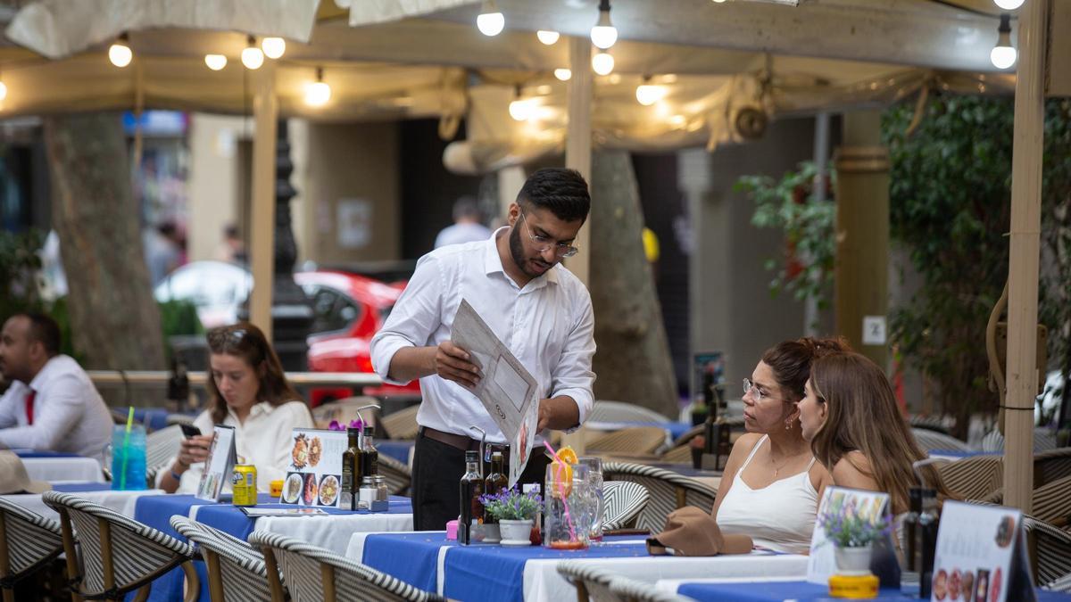 Un camarero atiende a unas clientas en una terraza, en Barcelona.