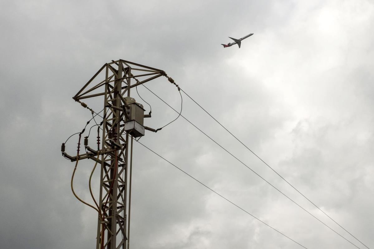 Un avión sobrevuela un poste de la luz.