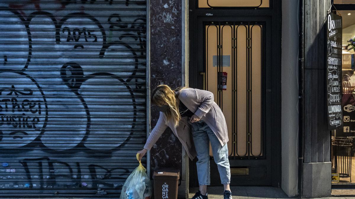 Una vecina deposita una bolsa y un cubo frente a un portal en la calle Gran de Sant Andreu.