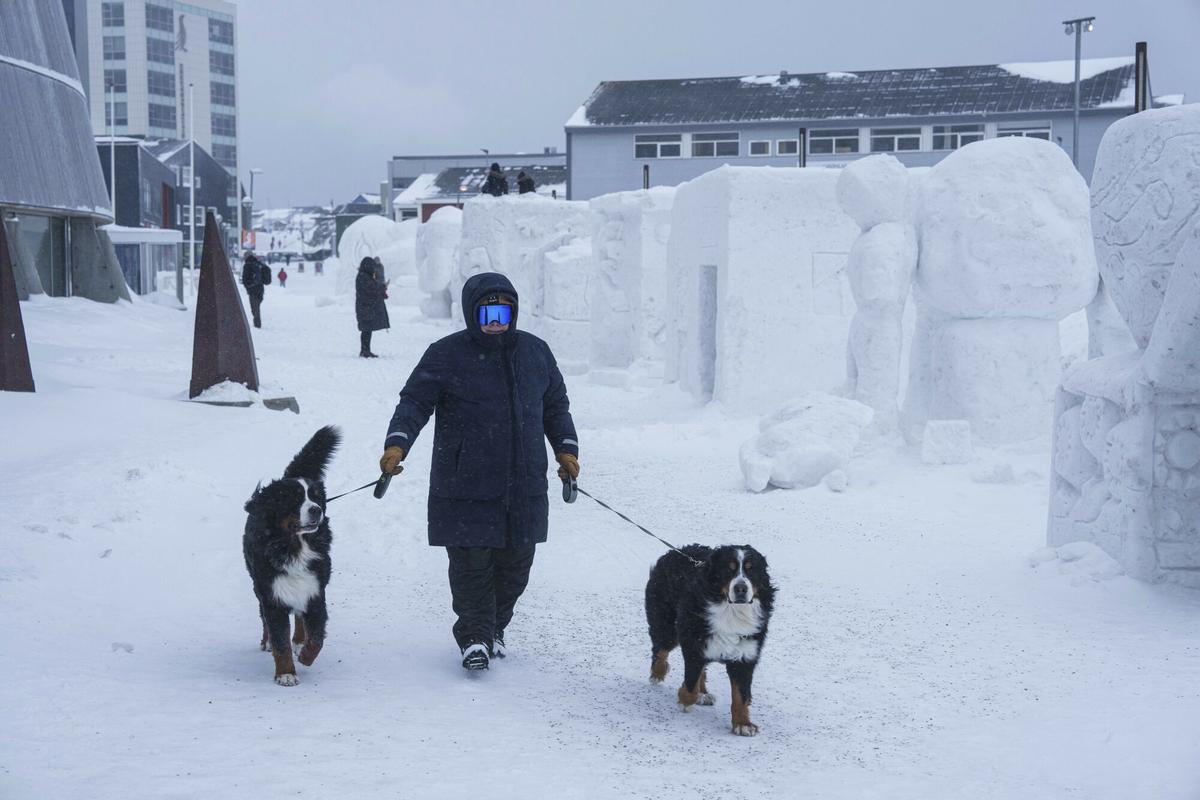 Un hombre camina con sus perros por una calle peatonal frente a esculturas de nieve en Nuuk, Groenlandia Un hombre camina con sus perros por una calle peatonal frente a esculturas de nieve en Nuuk, Groenlandia