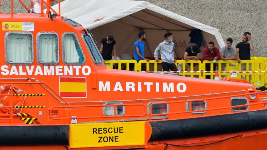 Un barco de Salvamento en el muelle de Arguineguín con migrantes en la parte posterior de la imagen