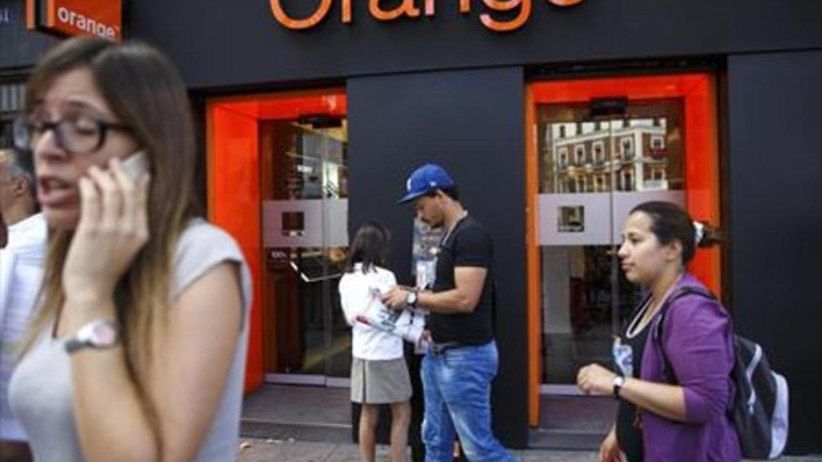 Personas pasan por delante de una tienda de Orange en Madrid.
