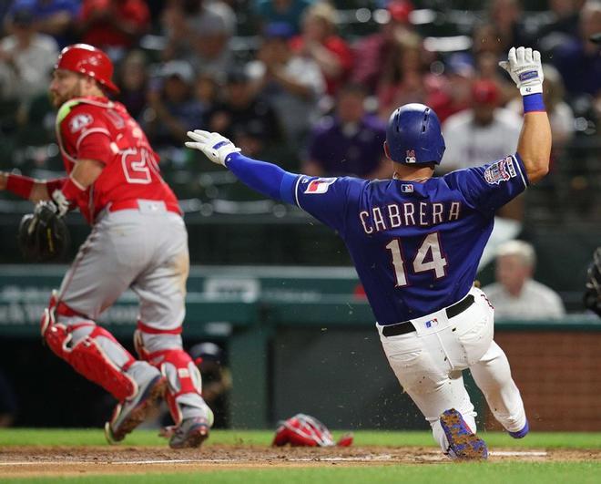 Asdrubal Cabrera # 14 de los Texas Rangers se desliza a casa para anotar en la quinta entrada contra Los Angeles Angels en Globe Life Park en Arlington, Texas.