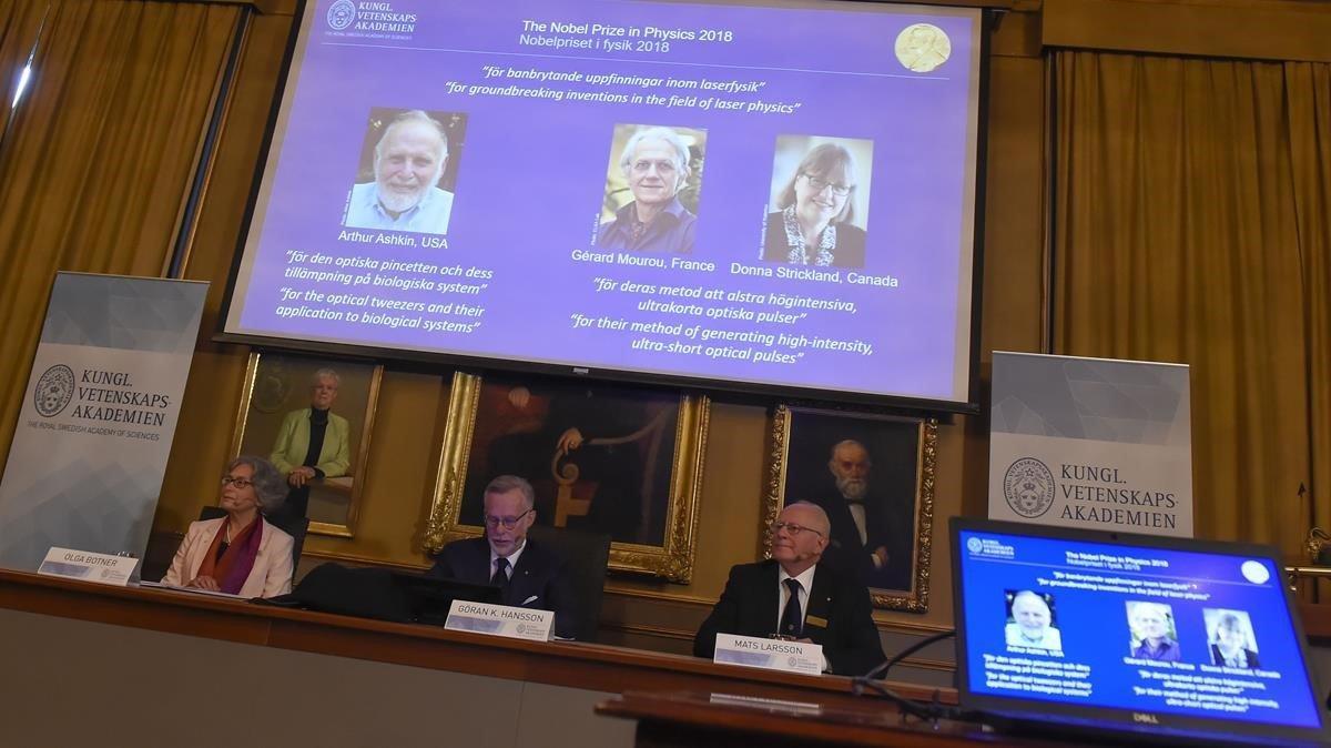 Los miembros del Comité Nobel de Física (LR) Olga Botner, Goran K Hansson y Mats Larsson se sientan frente a una pantalla que muestra los retratos de Arthur Ashkin de los Estados Unidos, Gerard Mourou de Francia y Donna Strickland de Canadá durante el anuncio de los ganadores del Premio Nobel de Física 2018 en la Real Academia de Ciencias de Suecia