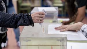 Una persona mete su voto en la urna en un colegio electoral.