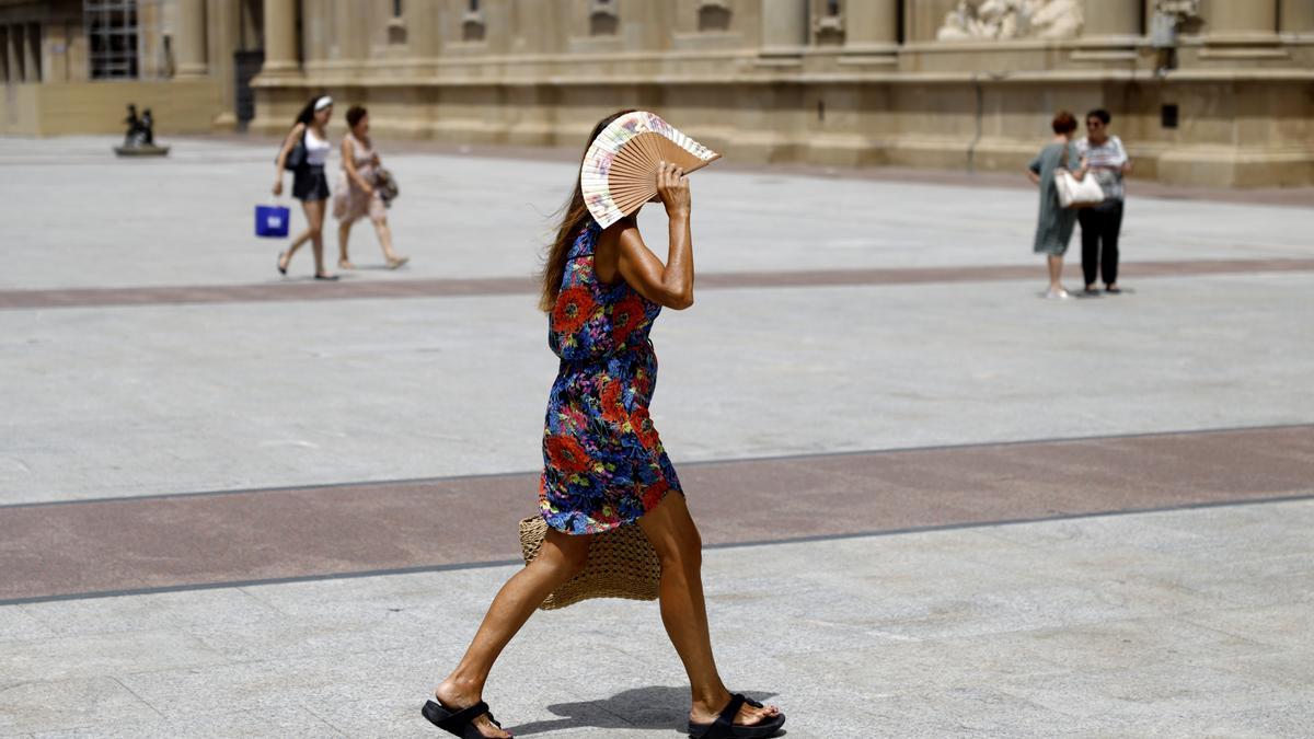 Una mujer se protege del sol mientras cruza la plaza del Pilar.