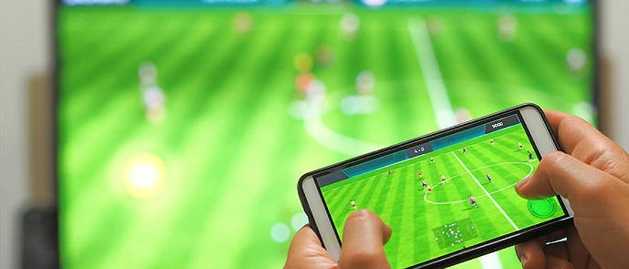 Una persona contempla su teléfono móvil mientras ve un partido de fútbol por la televisión.