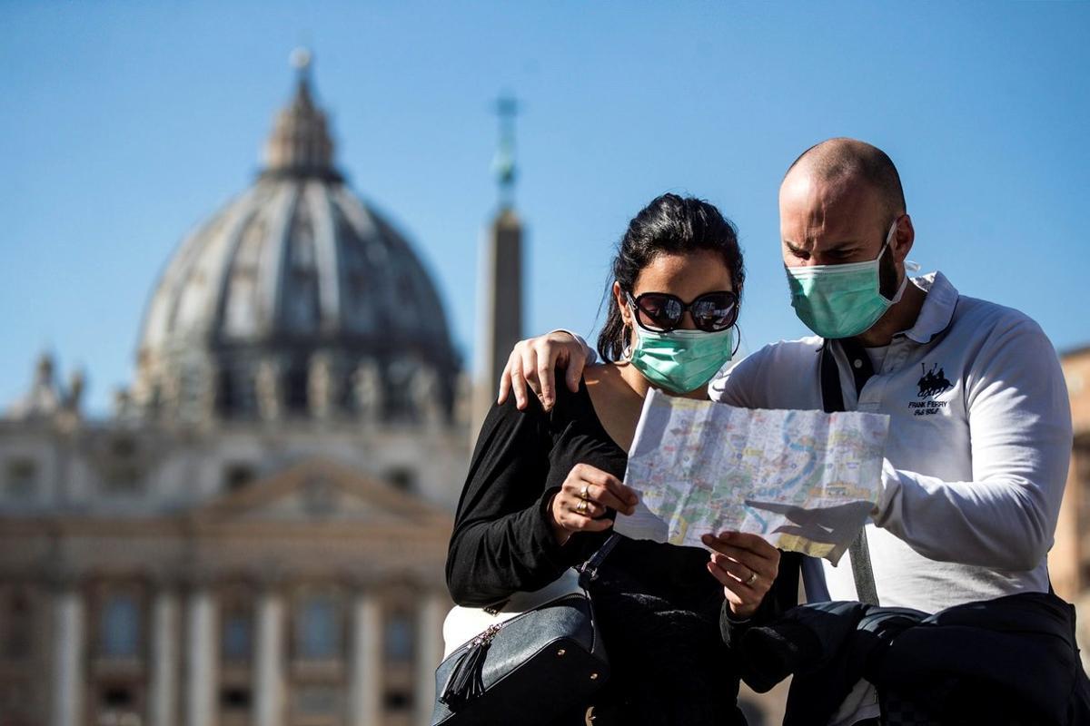 -FOTODELDÍA- EPA3768. CIUDAD DEL VATICANO, 24/02/2020.- Una pareja de turistas con máscaras faciales sanitarias visita la Plaza de San Pedro, este lunes en el Vaticano, donde se ha decidido cancelar algunos eventos programados en espacios cerrados para los próximos días tras el brote del coronavirus, que ha dejado seis muertos en Italia. EFE/ Angelo Carconi