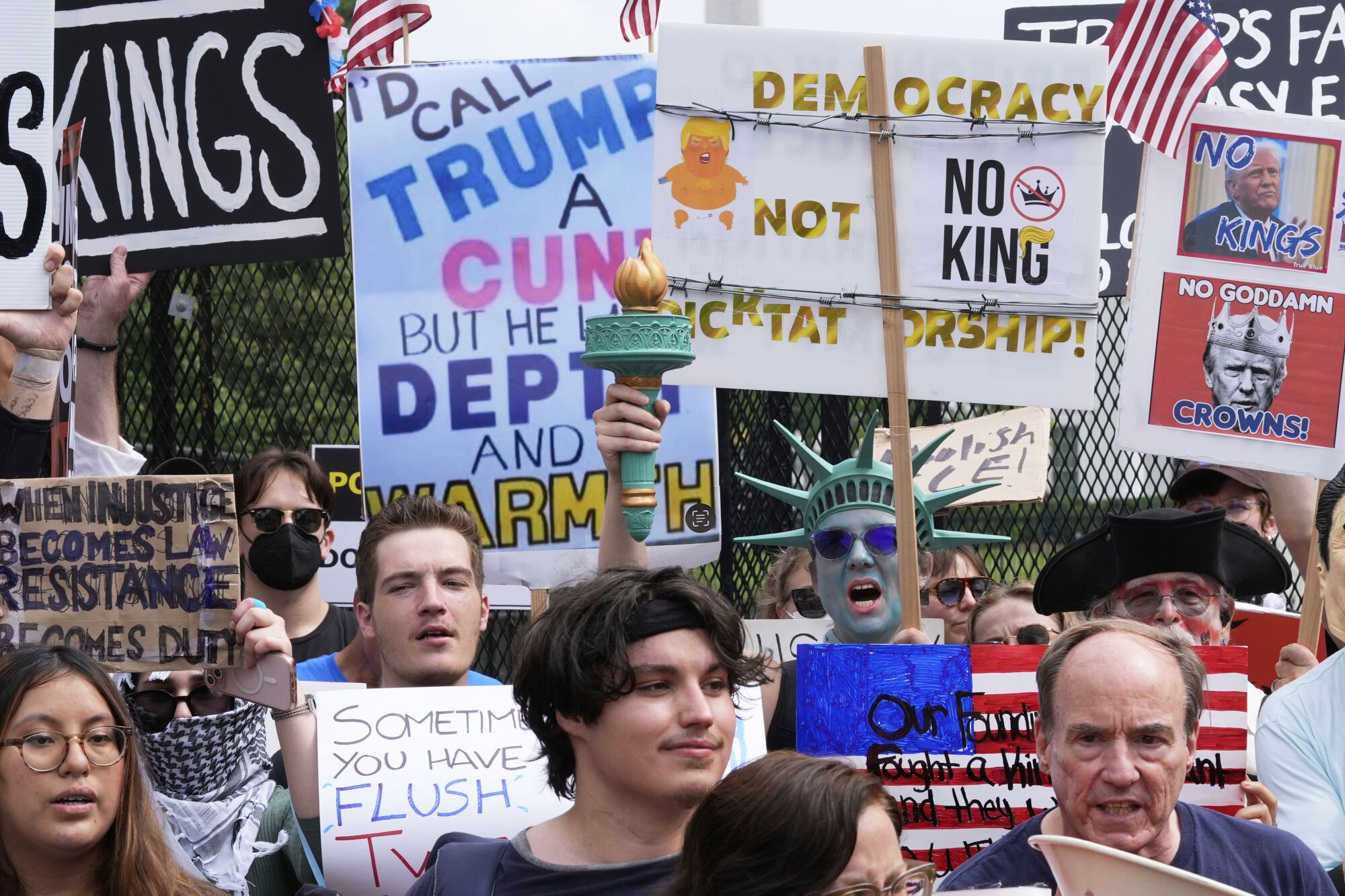 Demonstrators carrying signs stand near the White House during a protest taking place on the day of a military parade commemorating the Army's 250th anniversary, coinciding with President Donald Trump's 79th birthday, Saturday, June 14, 2025, in Washington. (AP Photo/Alex Brandon)