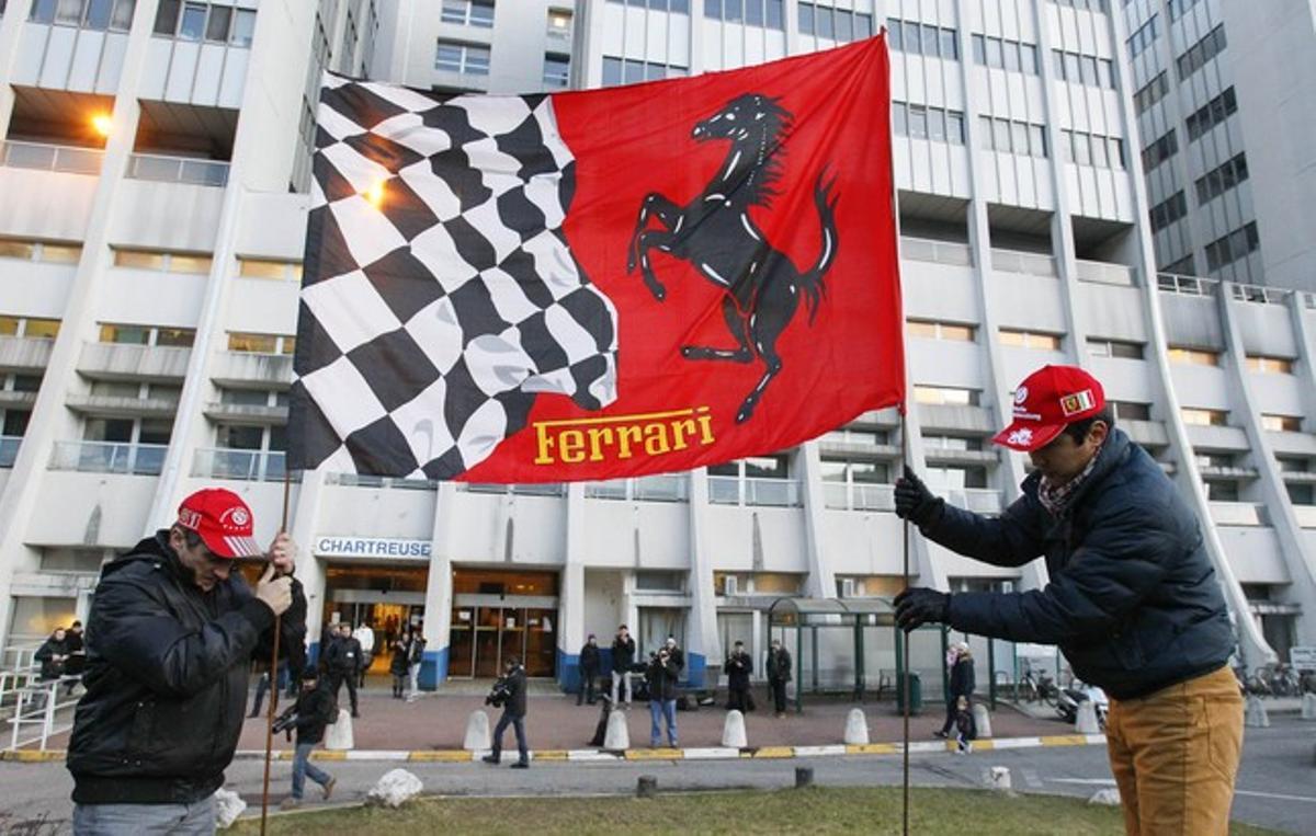 Dos fans planten una bandera de Ferrari davant l’hospital on està ingressat Schumacher, a Grenoble.