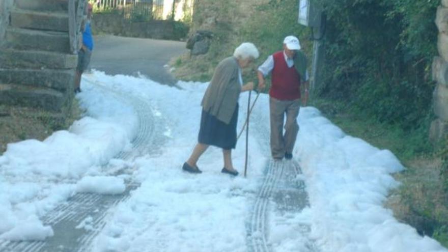 Dos vecinos de Quintana, observados por otro, caminan por una calle que conserva el manto de nieve.