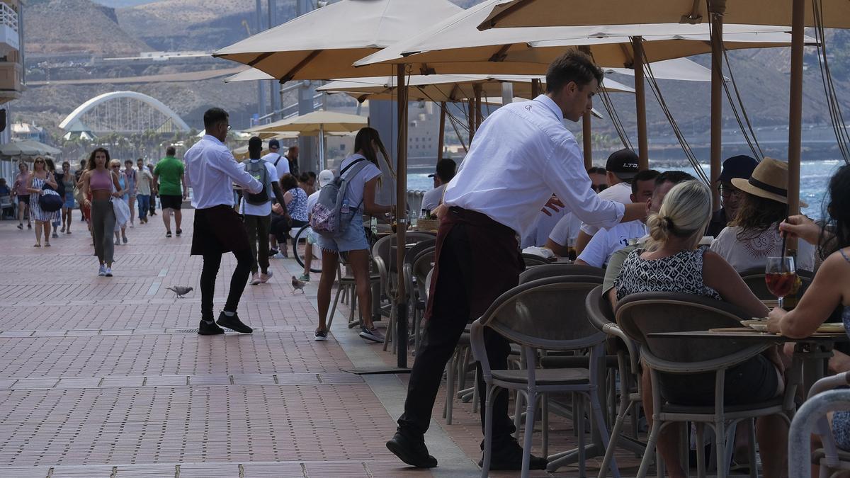 Varios camareros atienden las mesas de una terraza llena de clientes.