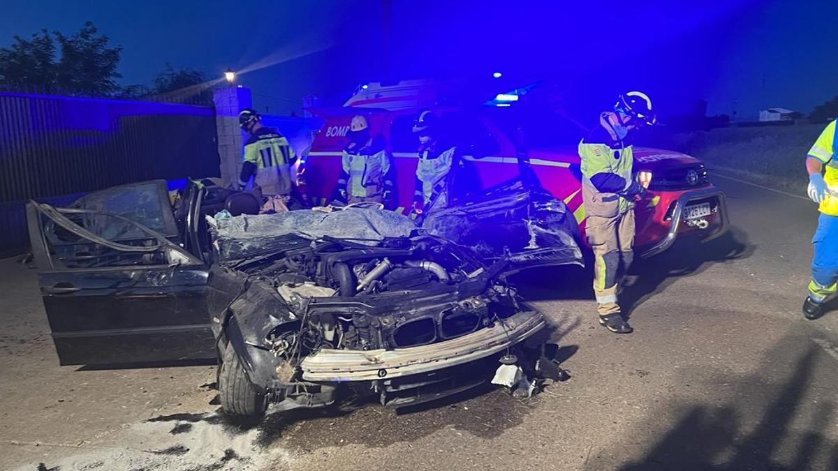 Uno de los turismos siniestrados y los bomberos trabajando en el lugar del accidente.