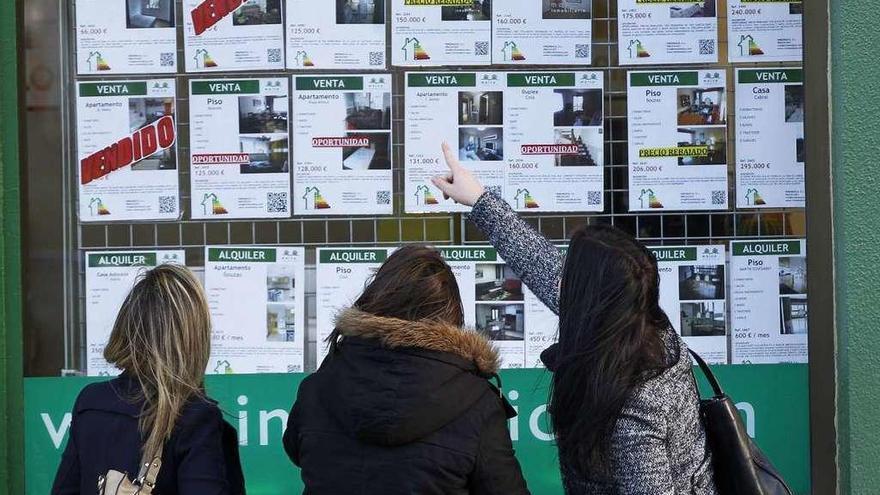 Tres mujeres observan los precios de venta de varias viviendas anunciadas en una inmobiliaria.