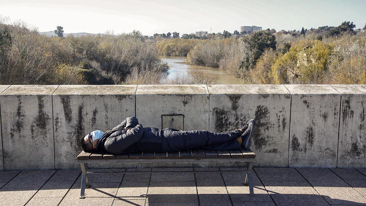 Un hombre toma el sol tumbado en un banco del Puente Romano.