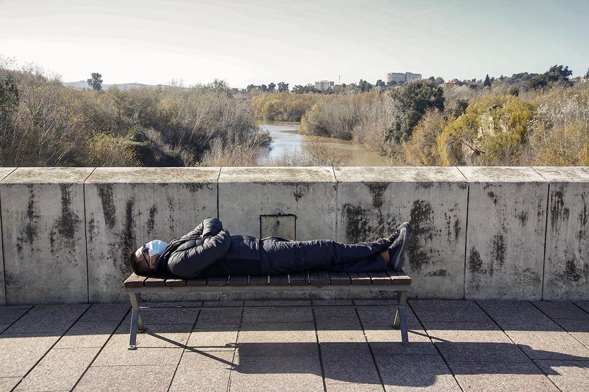 Un hombre toma el sol tumbado en un banco del Puente Romano.