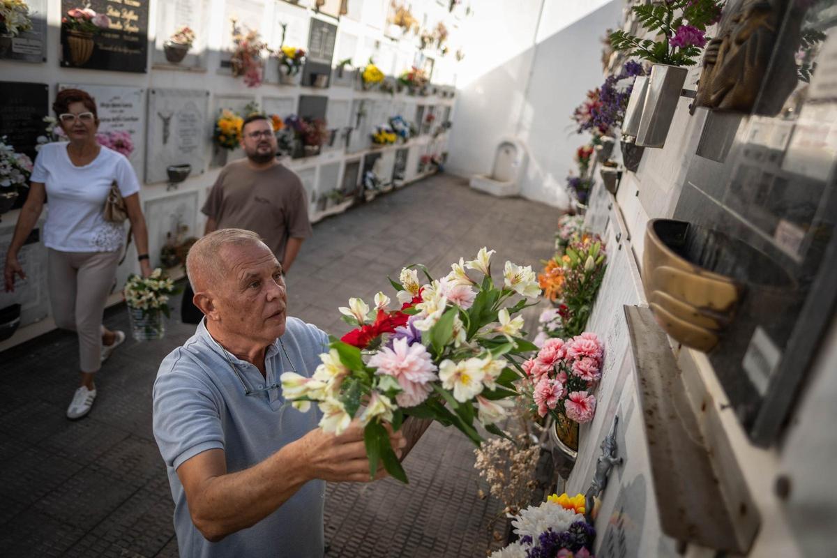 Leo Cortés arregla flores de un nicho en presencia de su esposa y nieto.