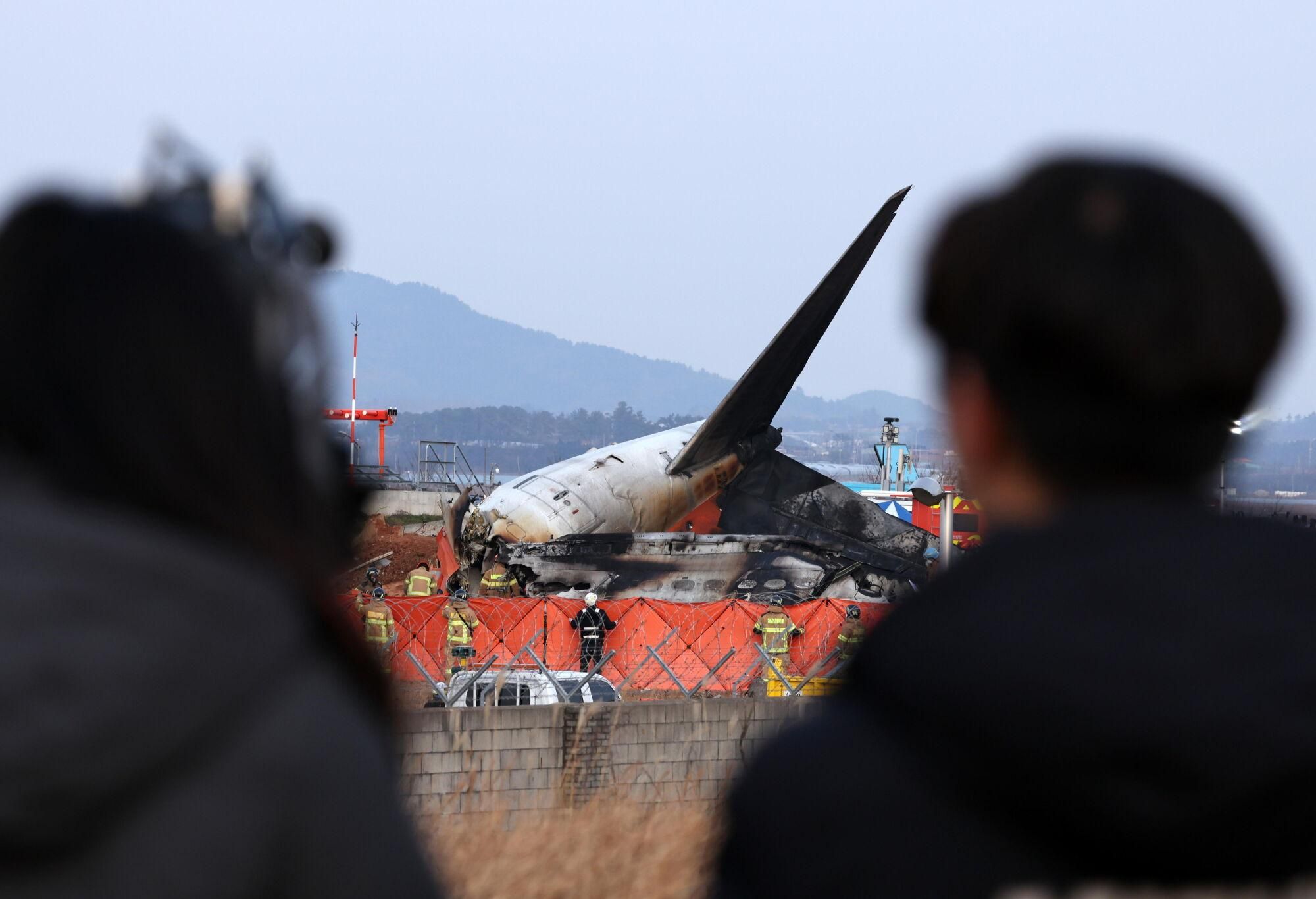 Muan (South Korea), 29/12/2024.- People look on as firefighters search at the wreckage of the Jeju Air aircraft at Muan International Airport in Muan, 288 kilometers southwest of Seoul, South Korea, 29 December 2024. According to the National Fire Agency, a passenger jet carrying 181 people erupted in flames after going off the runway at an airport in South Korea's southwestern county of Muan on 29 December, leaving at least 176 people dead. (Corea del Sur, Seúl) EFE/EPA/HAN MYUNG-GU