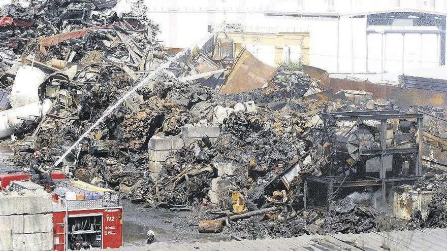 Los bomberos refrescan las últimas montañas de chatarra, debajo de las que todavía quedan rescoldos.