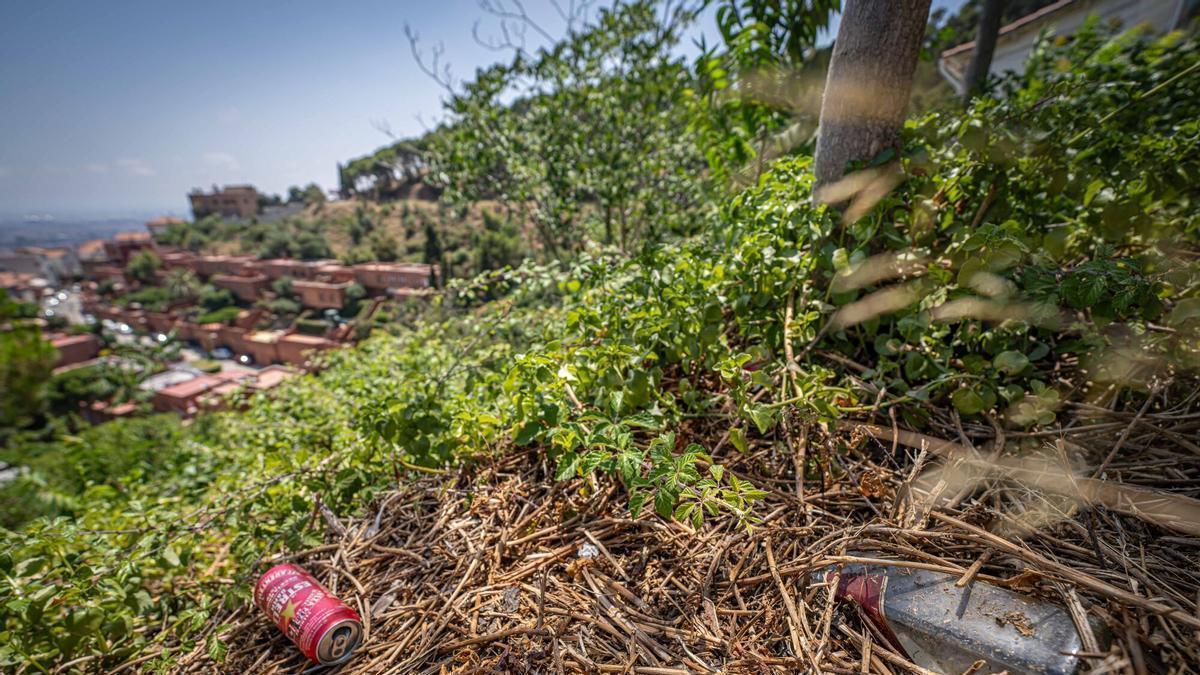 Zona de la carretera dels Aigües on, segons denuncien els veïns, se celebren botellons durant la nit. En la imatge, una ampolla de vidre abandonada al costat de nombroses burilles en una àrea on, asseguren, algunes persones també acampen i deixen residus que incrementen el risc d'incendi al parc natural de Collserola. Barcelona, 14 de juliol de 2026. AUTOR: Manu Mitru | EPC