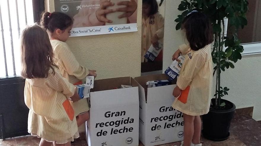 Tres niños depositando bricks de leche en esta iniciativa solidaria.