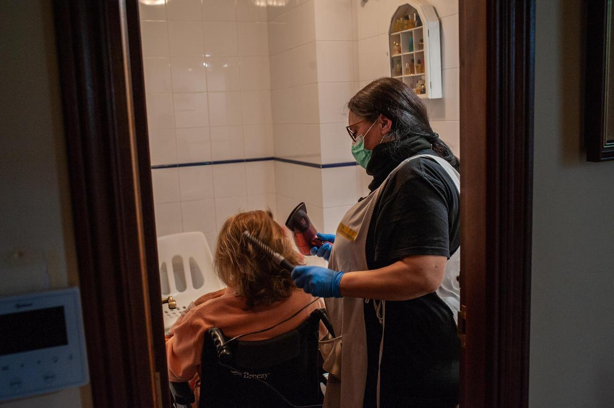 Una trabajadora de ayuda en el hogar peina a una anciana en su domicilio