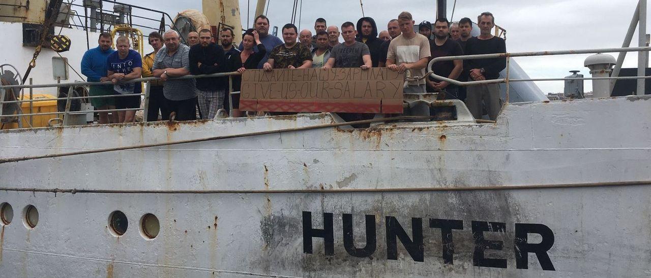 Parte de la tripulación del &#039;Hunter&#039; muestra un cartel reclamando el pago de sus salarios.
