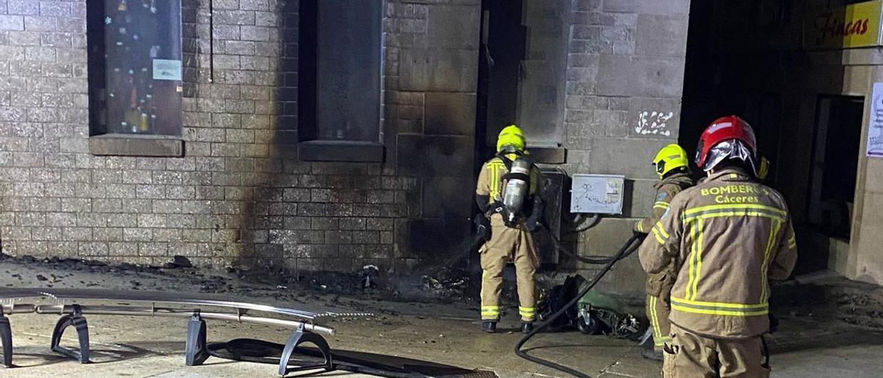 Bomberos ante el edificio dañado por la quema de contenedores en Plasencia.