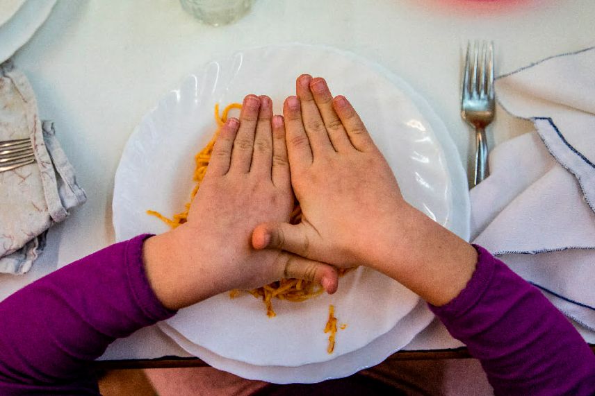 Un niño tapa con las manos su plato de pasta.