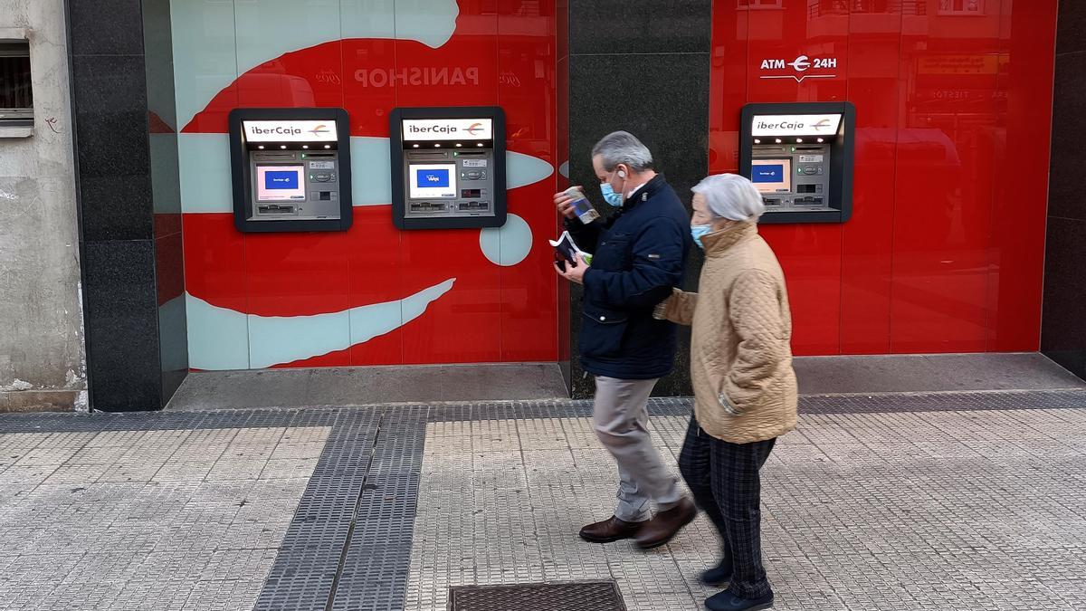 Dos personas mayores pasan por delante de un cajero automático en Zaragoza