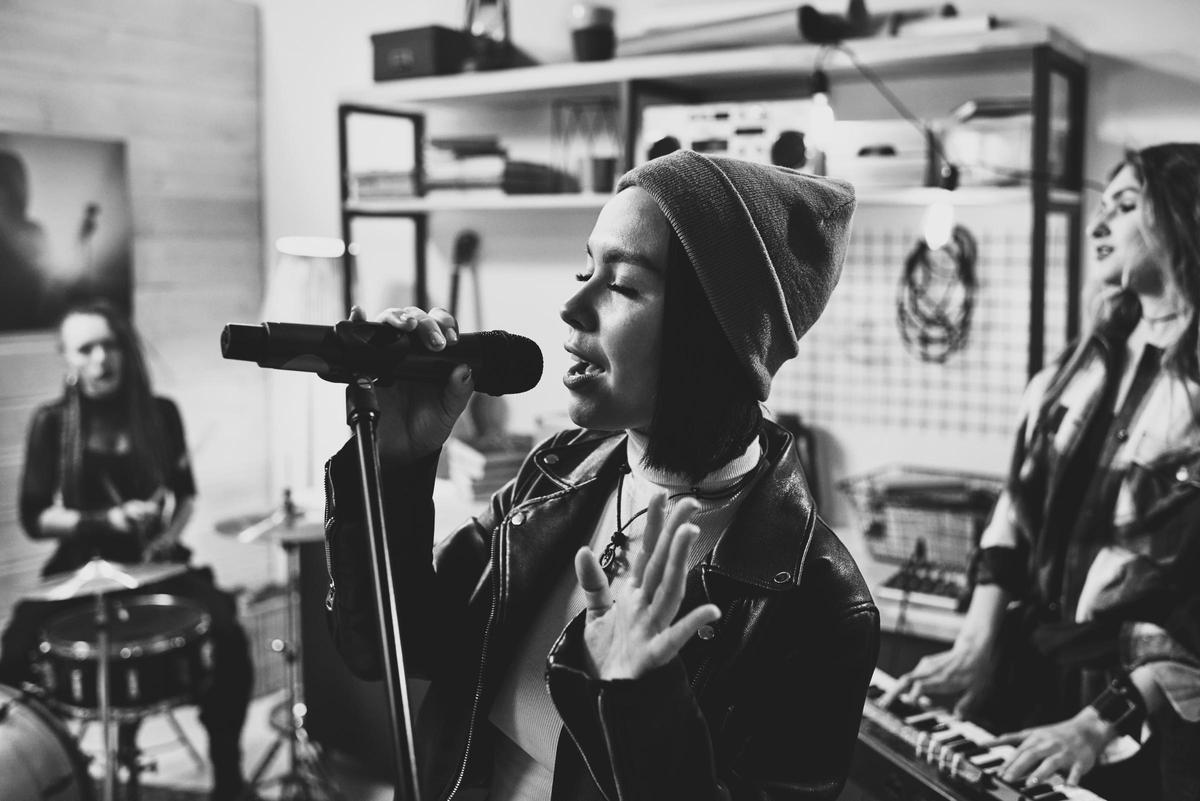 Young pretty female musician recording songs with band in studio