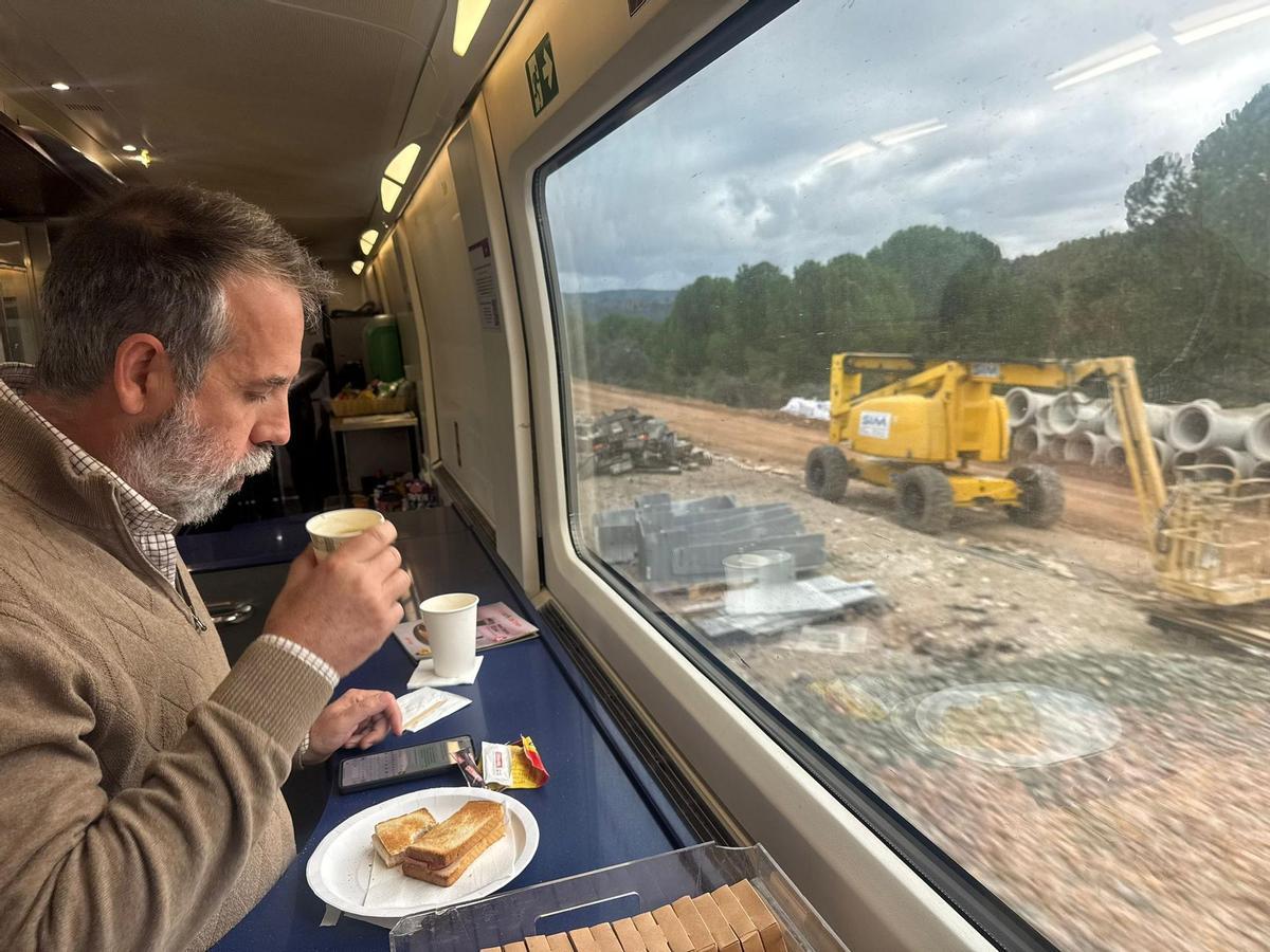 Un viajero toma su desayuno en un tren AVE entre Córdoba y Madrid, este martes por la mañana, mientras observa una máquina trabajando junto a las vías.