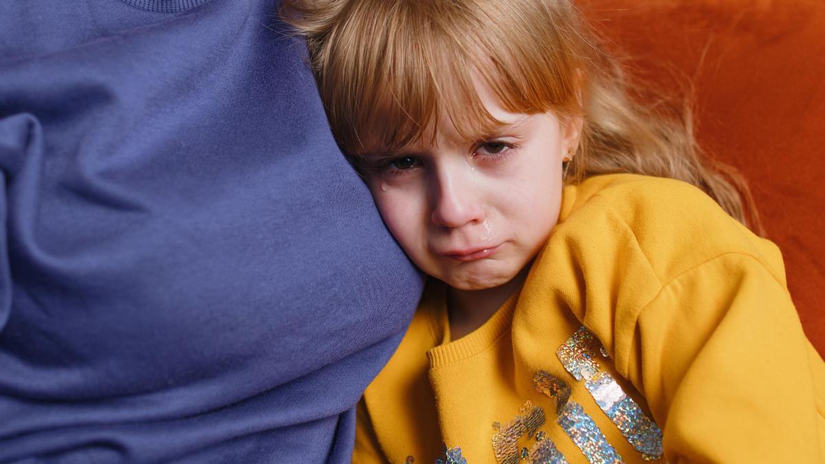 Una niña llorando junto a un adulto.