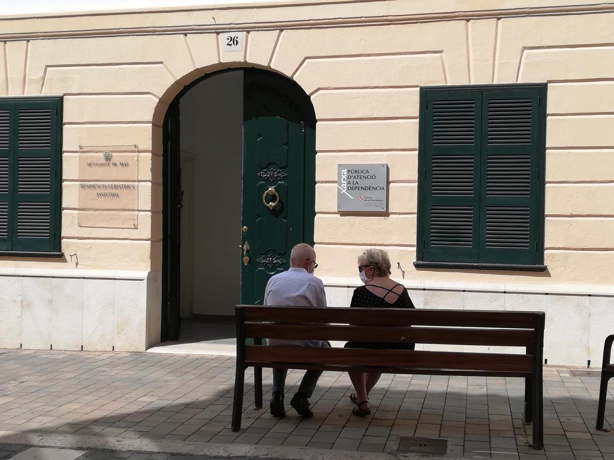 Archivo - Dos personas mayores conversan sentadas en un banco y con mascarilla, ante una Residencia