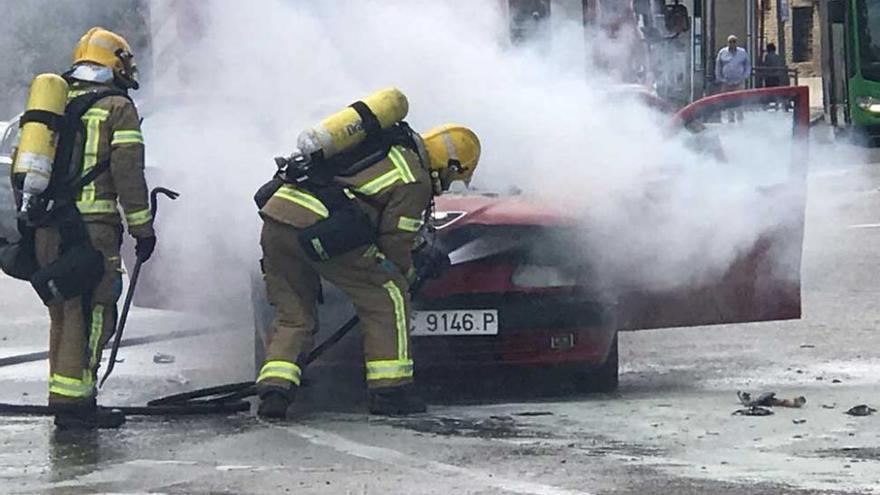 Los bomberos sofocan un incendio en un coche frente a la plaza de toros de Cáceres