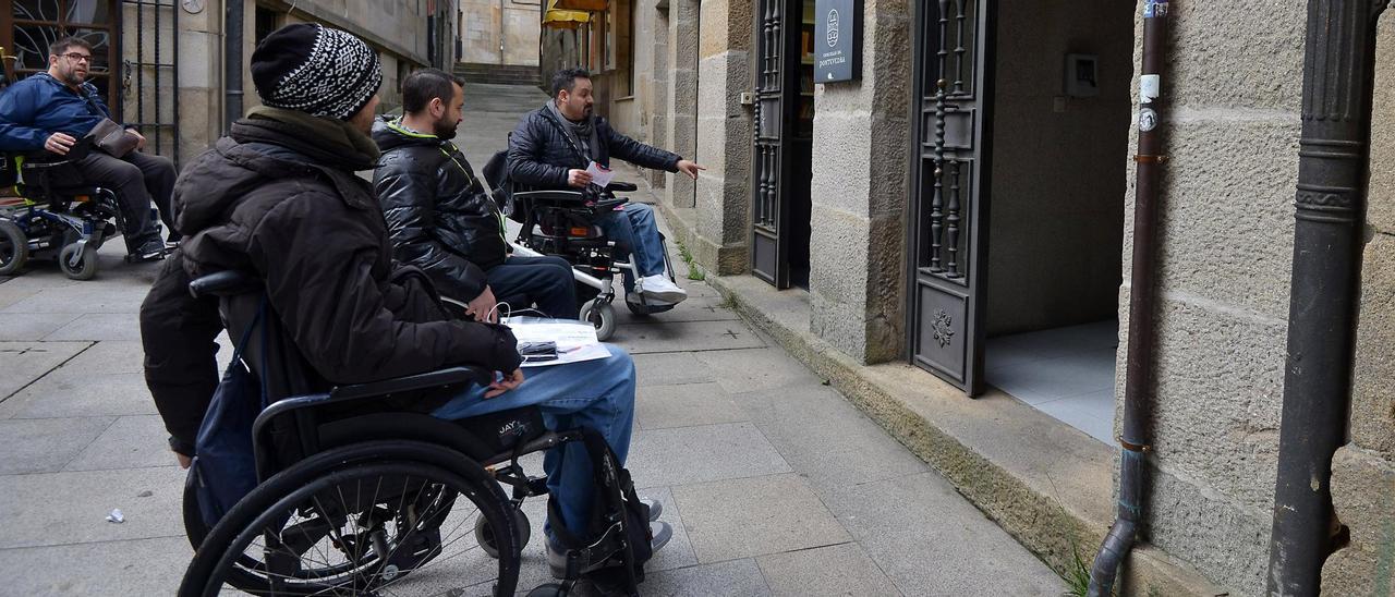 Personas en silla de ruedas intentan entrar a un edificio con barreras arquitectónicas.