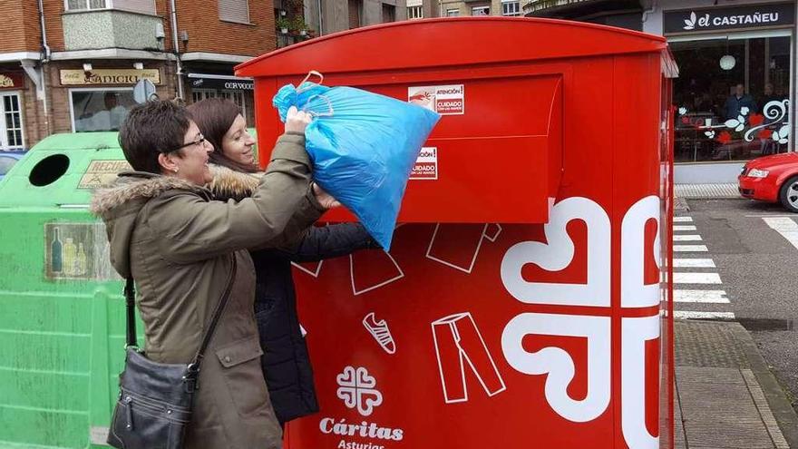 María José Llaneza y Aida Rodríguez depositan una bolsa de ropa en el contenedor de Cáritas.