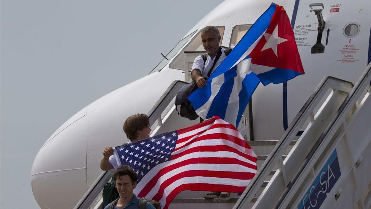Dos pasajeros descienden de un avión en Santa Clara (California, EEUU) con sendas banderas de Estados Unidos y Cuba, en agosto de 2016