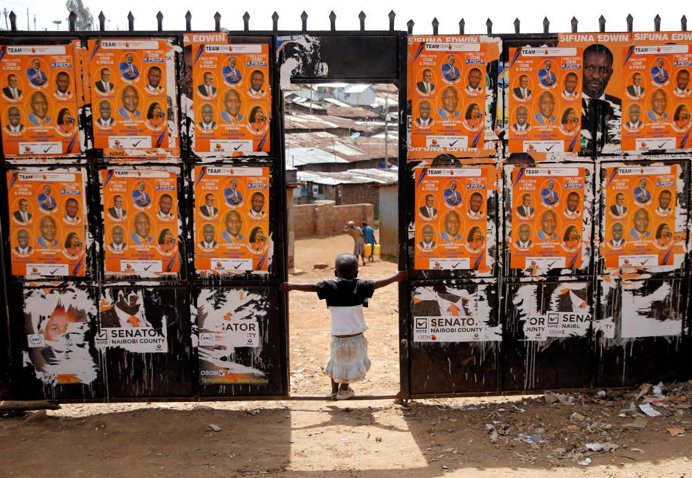 Un niño juega en la entrada a una mesa de votación llena de carteles de la campaña en la sala de Sarang'ombe antes de la elección presidencial en la aldea de Kisumu Ndogo en los barrios bajos de Kibera de Nairobi, Kenia