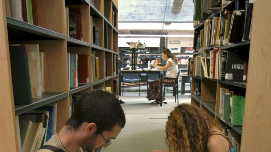 Dos estudiantes universitarios consultan unos libros en una biblioteca.