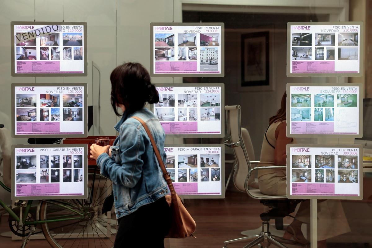 Una joven mira el escaparate de una agencia inmobiliaria.