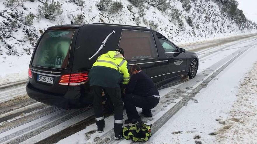 Un agente de la Guardia Civil ayuda a poner las cadenas a un conductor de un coche fúnebre en Triacastela.