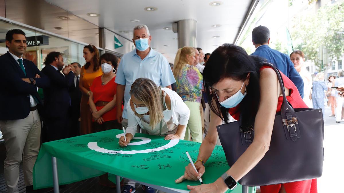 Firma de la bandera de la Asociación Española Contra el Cáncer antes de ser izada frente al Corte Inglés