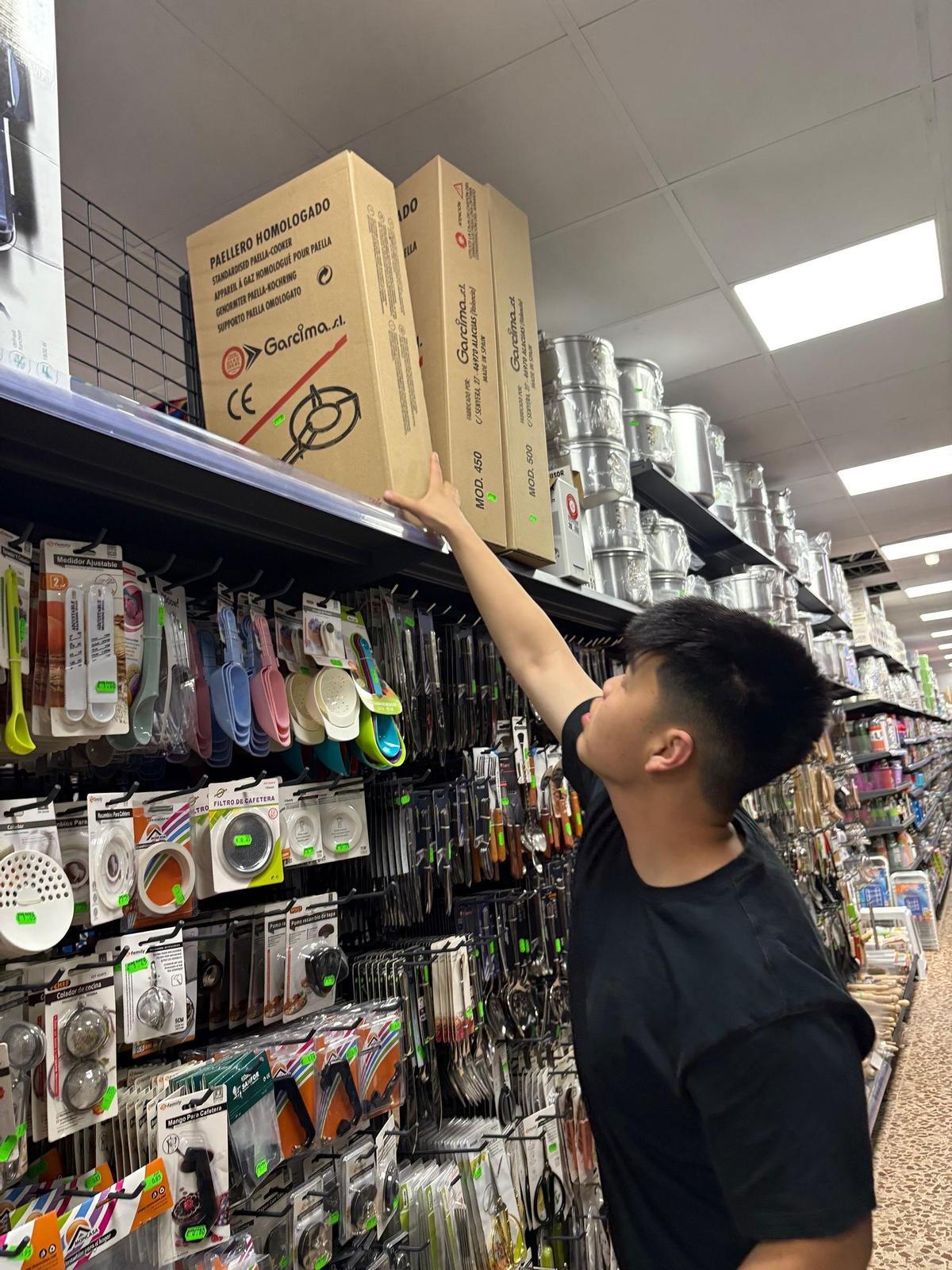 El hijo de los responsables de un bazar chino muestra los paelleros de gas, entre los productos más vendidos.