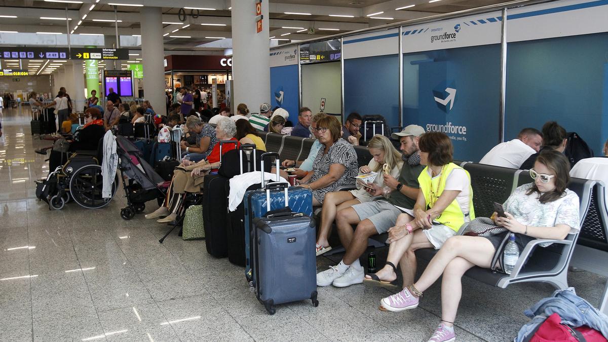 Varios turistas esperan sentados con sus maletas en el aeropuerto de Palma.