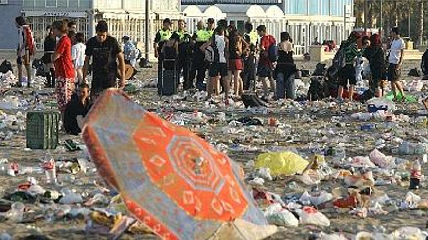 restos en la arena. Un grupo de policías locales piden a los jovenes que abandonen la playa para limpiarla.