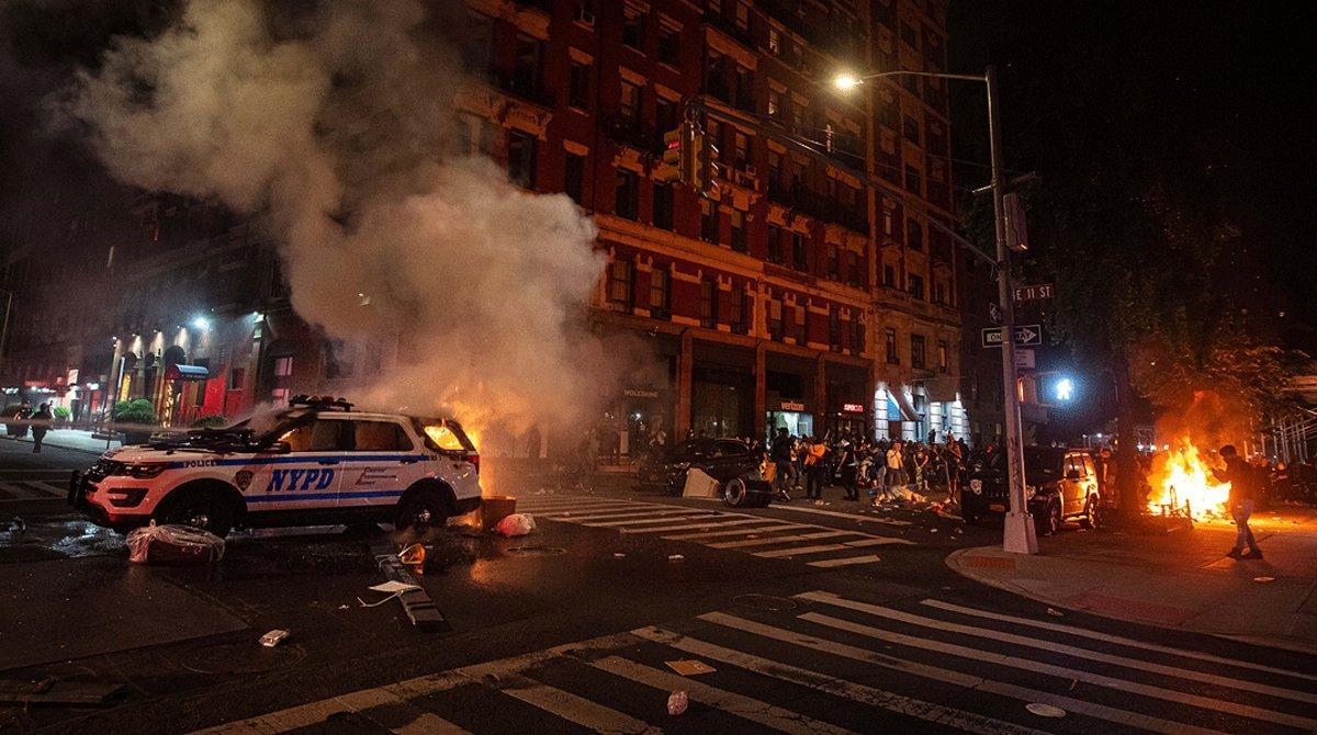 Un numeroso grupo de manifestantes observan cómo arde un coche de la policía en Manhattan, este sábado 30 de mayo, durante las protestas por la muerte de George Floyd en Minneápolis.  