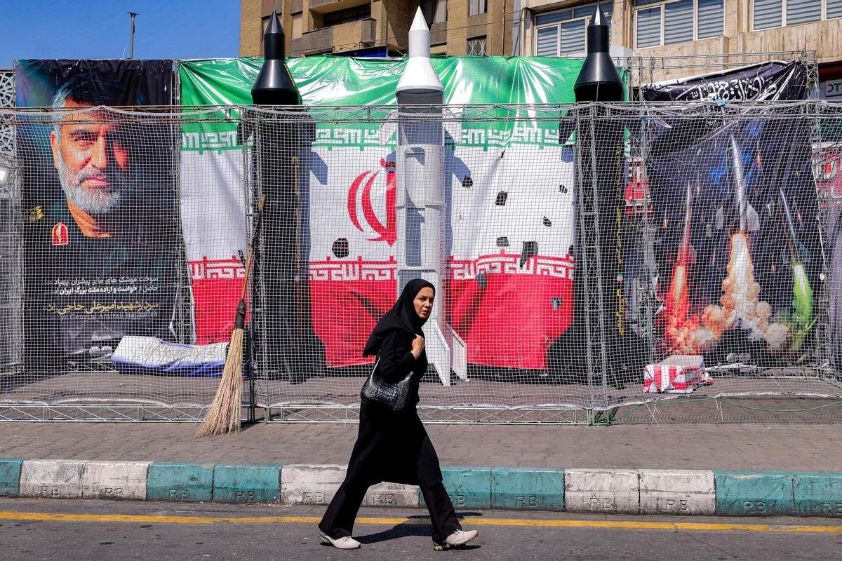A woman walks past mockups of Iranian missiles along Valiasr Square in Tehran on April 6, 2026. Israeli strikes killed the intelligence chief of Iran's Revolutionary Guards, as the Islamic republic on April 6 defied threats from the US President to devastate civilian infrastructure if it does not reopen the Strait of Hormuz. (Photo by ATTA KENARE / AFP) /. SEE CAPTION FOR MORE INFORMATION / Attention editors: Photo taken with approval from the Ministry of Culture and Islamic Guidance (Ershad) -- AFP covers the war in the Middle East through its extensive regional network, including bureaus in Tehran, Jerusal